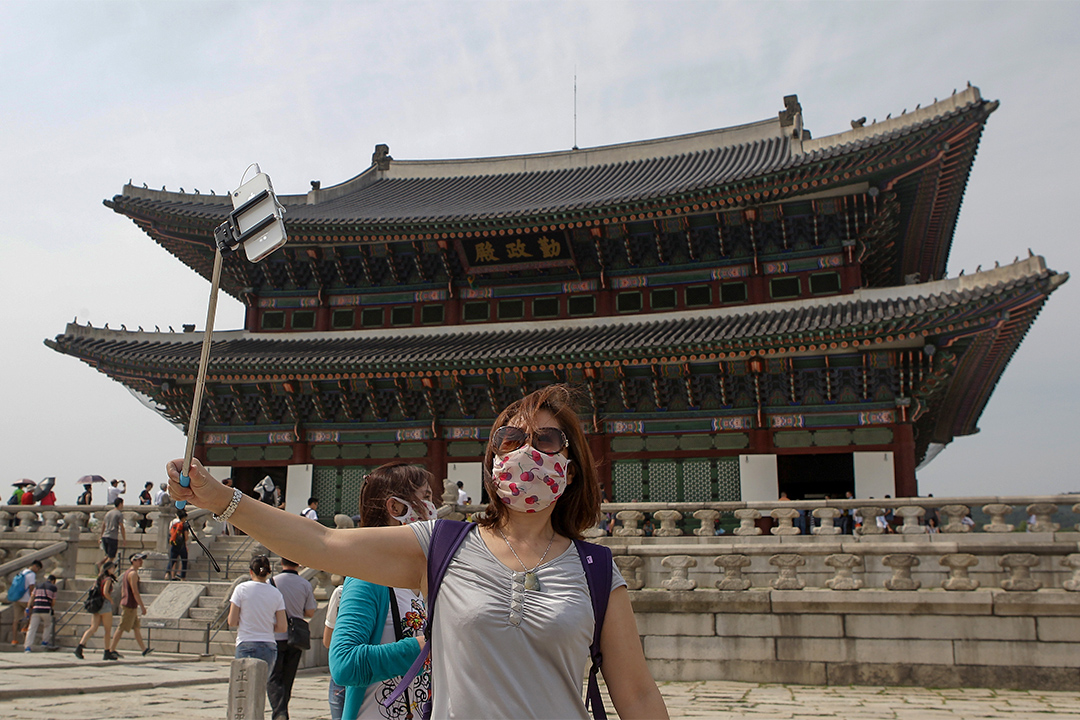 2015年,因“新沙士”影响了韩国旅游业。图为2015,游客带著口罩于韩国景点景福宫外拍照。