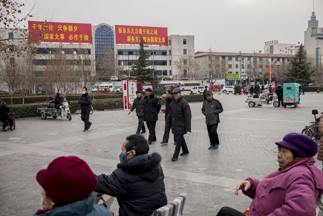 市民在雄县政府大楼前的广场消磨时间,背后有设立河北雄安新区的大字标语。