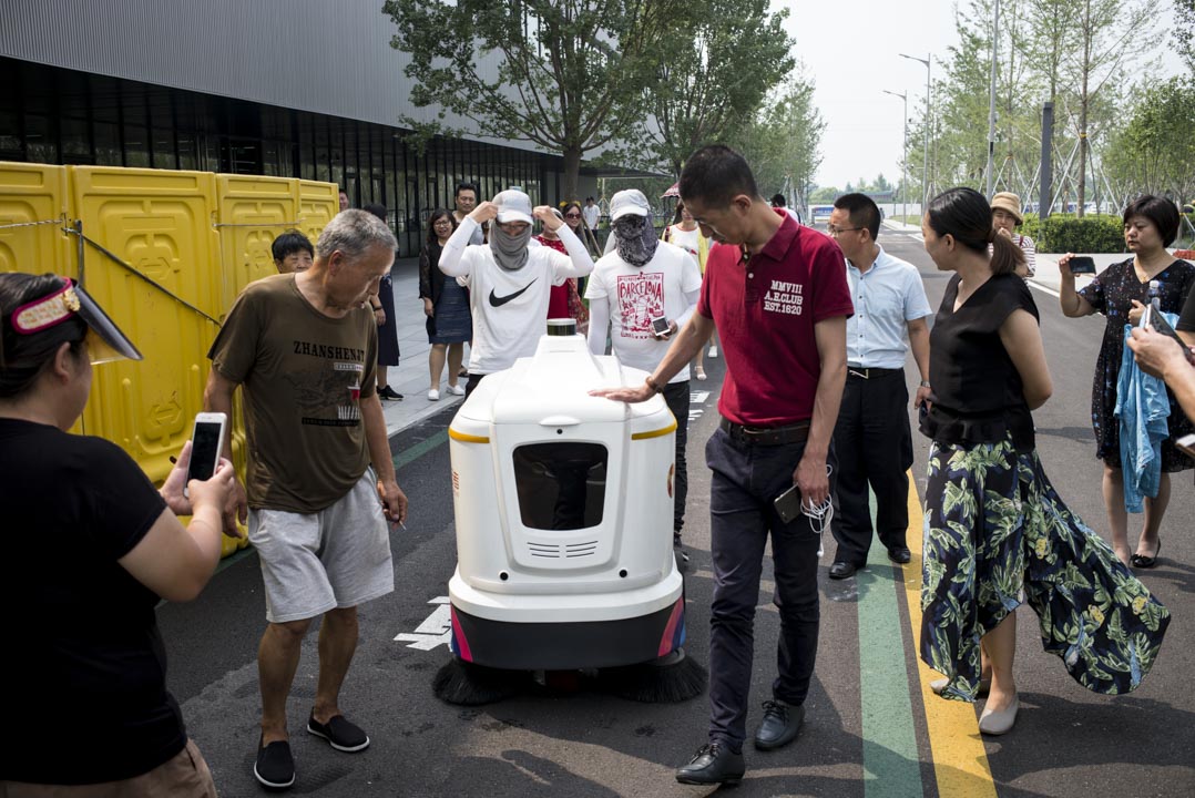 人群圍住了一輛正在運行的「無人駕駛掃路機」。