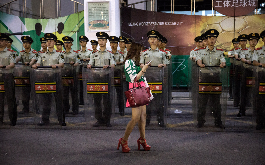 足球場外,一名使用智能電話的女子在武警面前經過。