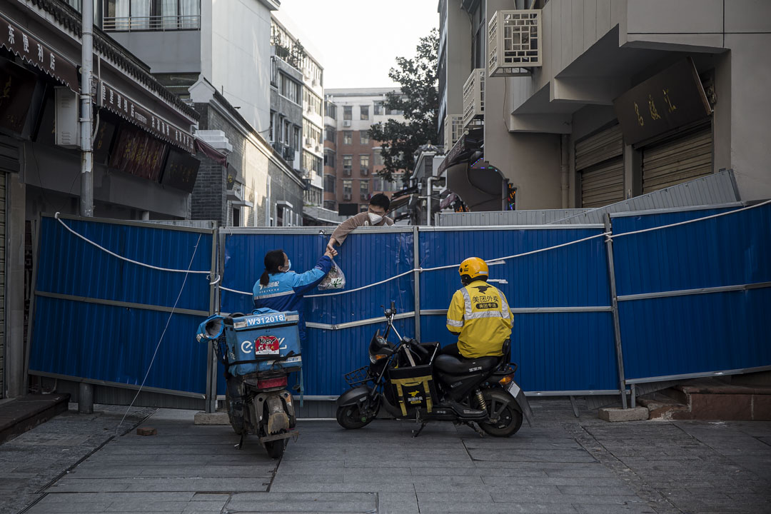 武漢戶部巷社區,送餐員將外賣遞給圍欄內的居⺠。