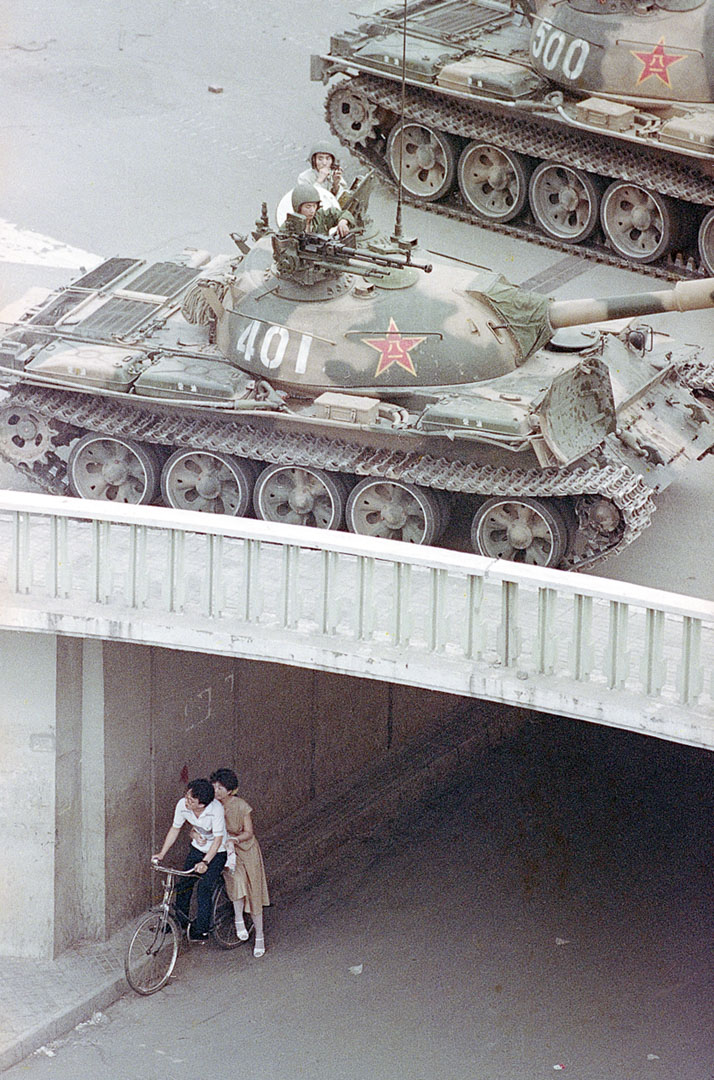 1989年6月5日,一对中国情侣骑着单车以地下通道作掩护,坦克在桥上行走。