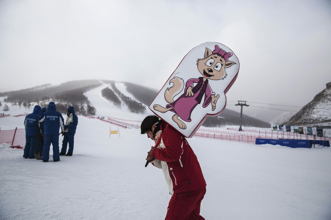 2016年1月21日,河北崇禮,一名工人在新建的太舞滑雪場舉著標牌。