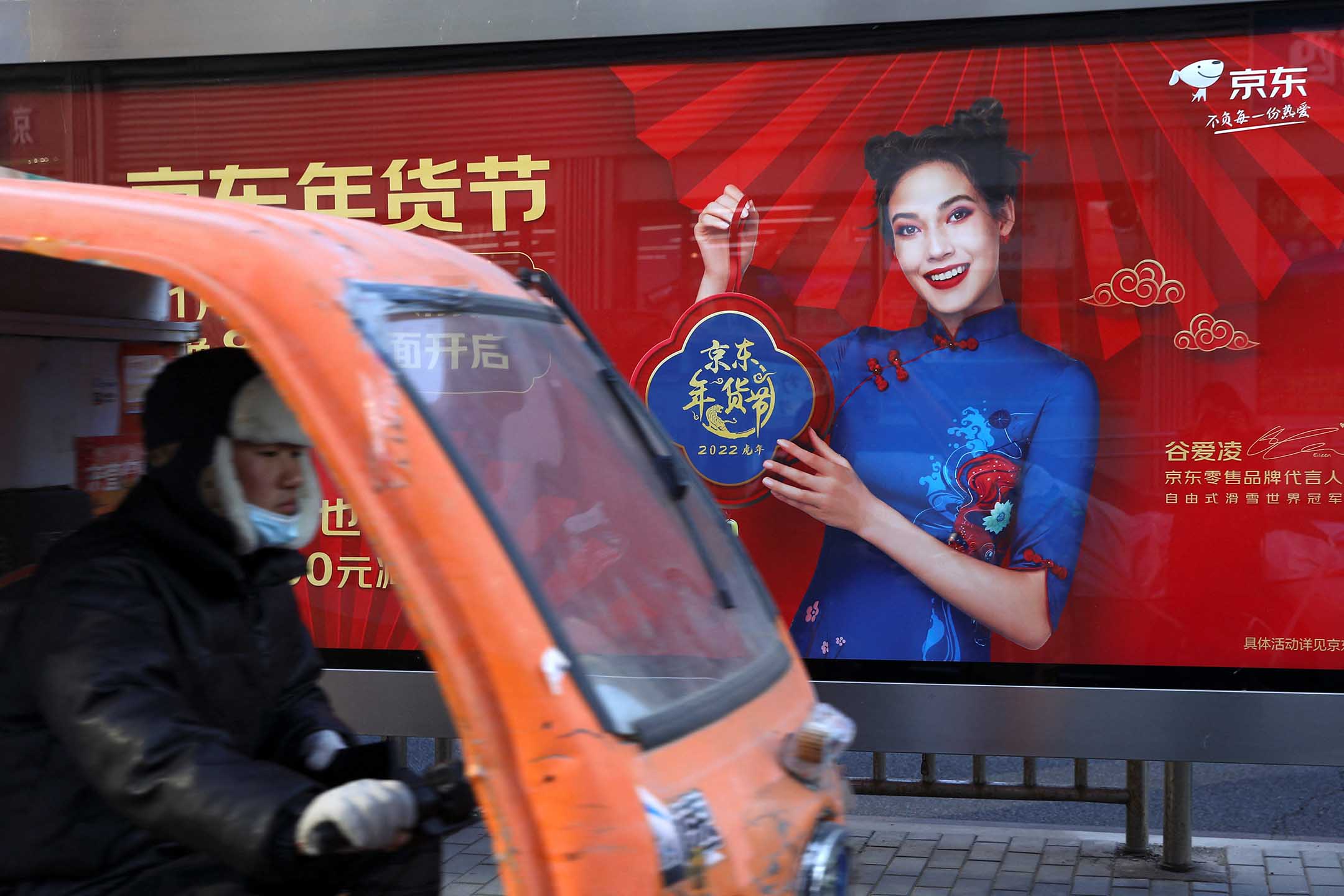 2022年1月11日中国北京,一名送货员骑著一辆车经过一个公共汽车站内谷爱凌的广告。