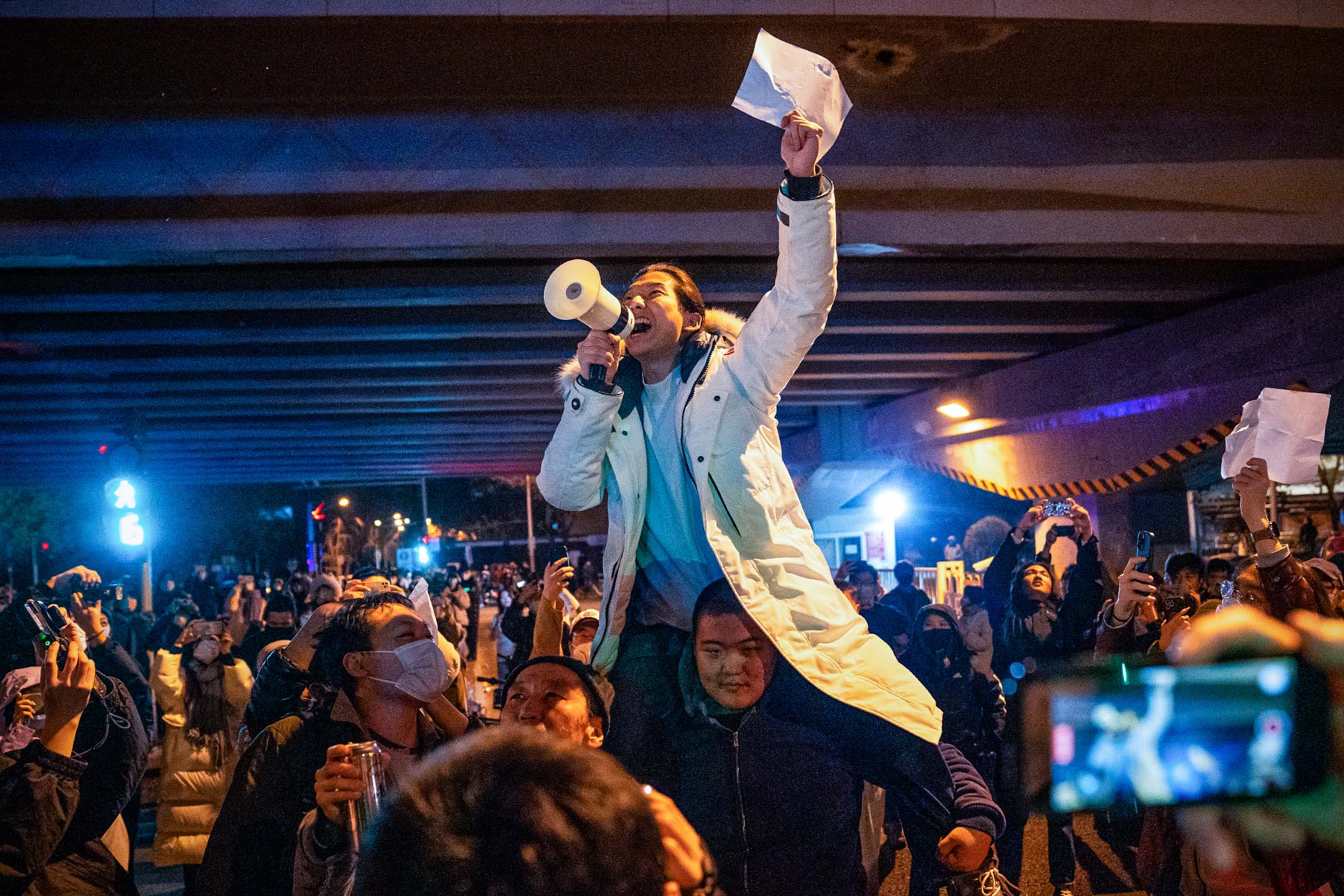 2022年11月28日,北京的示威活動中,一名示威者舉著白紙並高喊口號。在街頭和大學校園,反對封控的抗議蔓延中國各地。