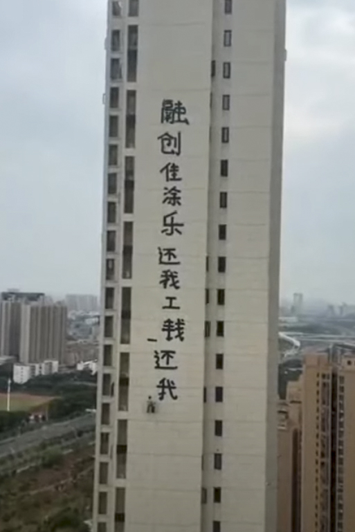一位工人吊着绳索在一座住宅楼的外墙上刷标语,内容为“融创佳涂乐还我工钱,还我血汗钱”,结尾还画了两只乌龟。