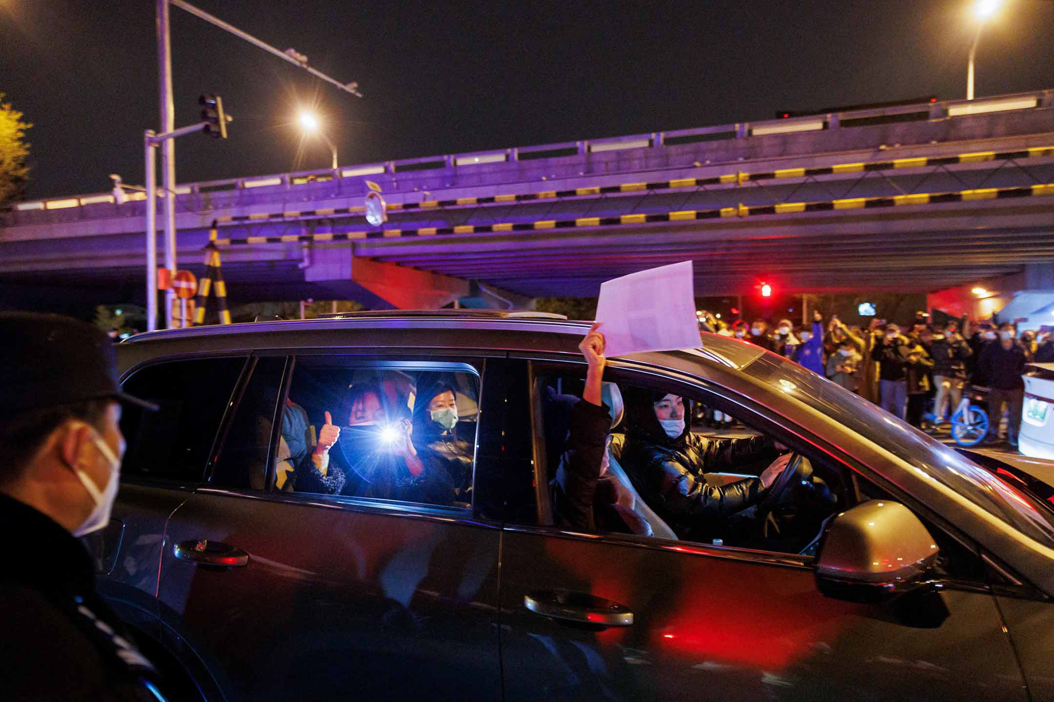 2022年11月28日,北京,為烏魯木齊火災受害者守夜後的集會上,一名車內的人拿著一張白紙抗議。