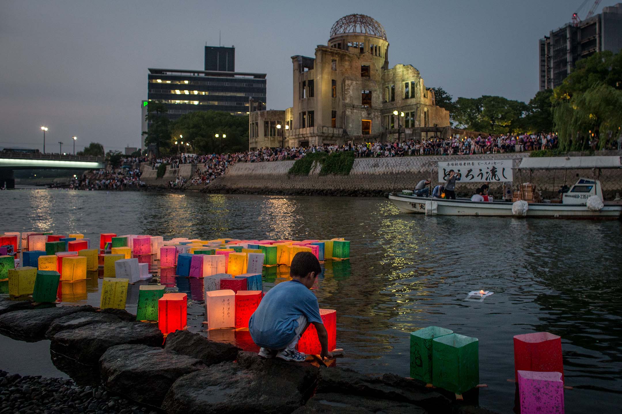 2015年8月6日,日本广岛,一名男孩在当年原子弹的爆炸现场,漂浮蜡烛点燃的纸灯笼,纪念当年的遇难者。摄:Chris McGrath/Getty Images