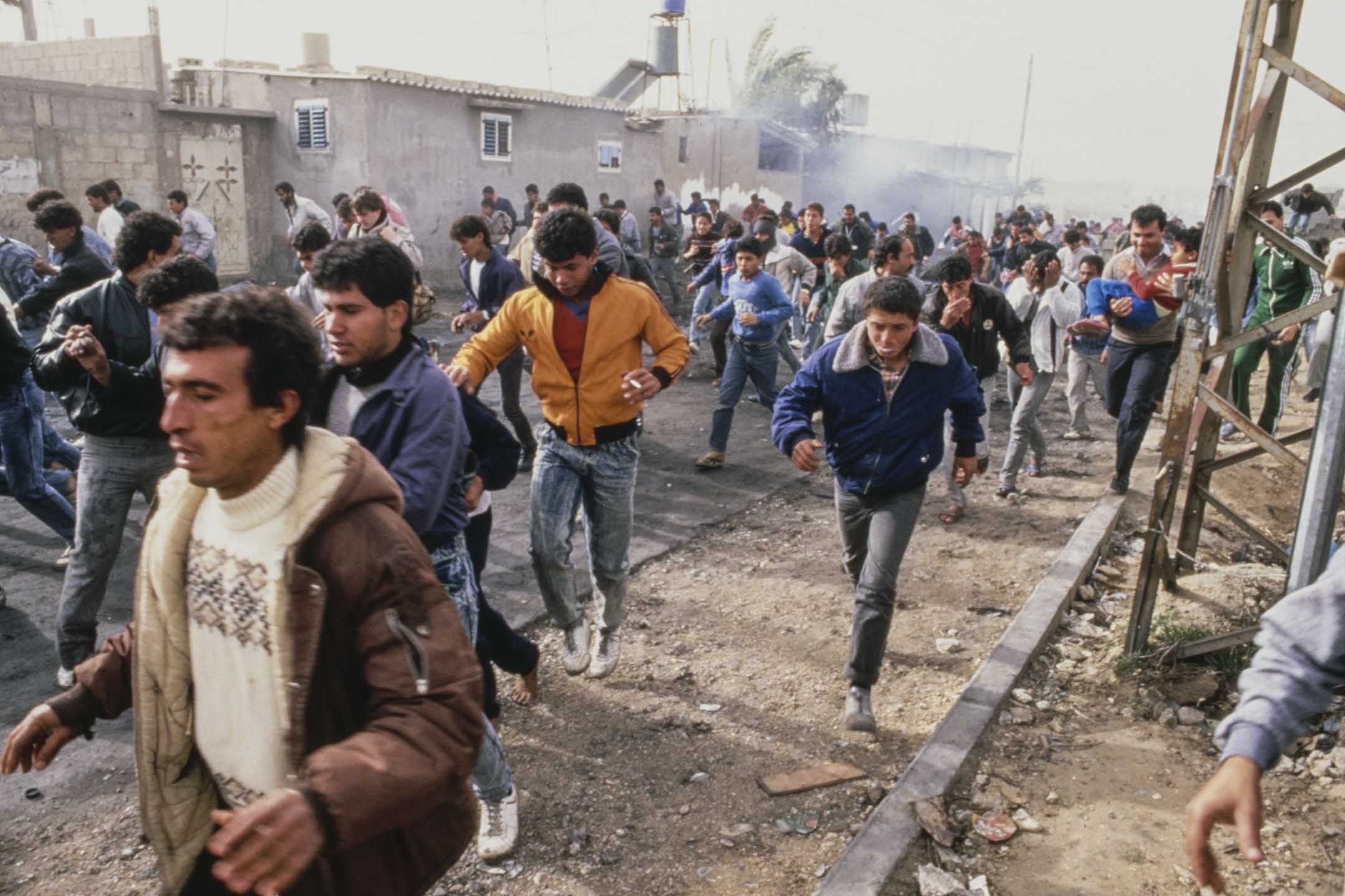 1987年12月22日,巴勒斯坦加沙,第一次巴勒斯坦起義期間,人們在街道上逃離煙霧。攝:Derek Hudson/Getty Images