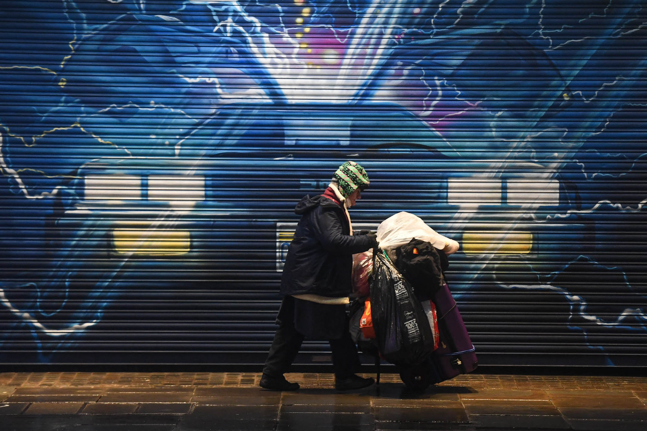 2020年12月13日,英國倫敦,一名無家者經過一幅壁畫前。攝:Peter Summers/Getty Images