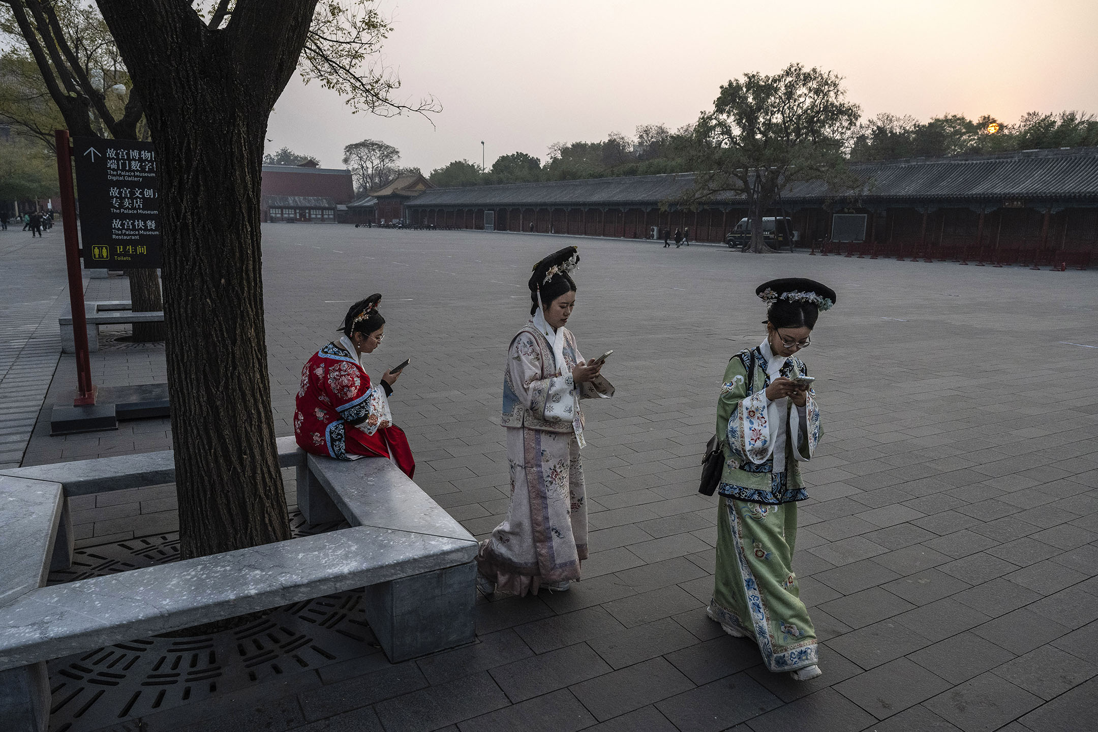 2023年11月21日,北京紫禁城外,身著清宮服裝的婦女們看著手機。攝:Kevin Frayer/Getty Images