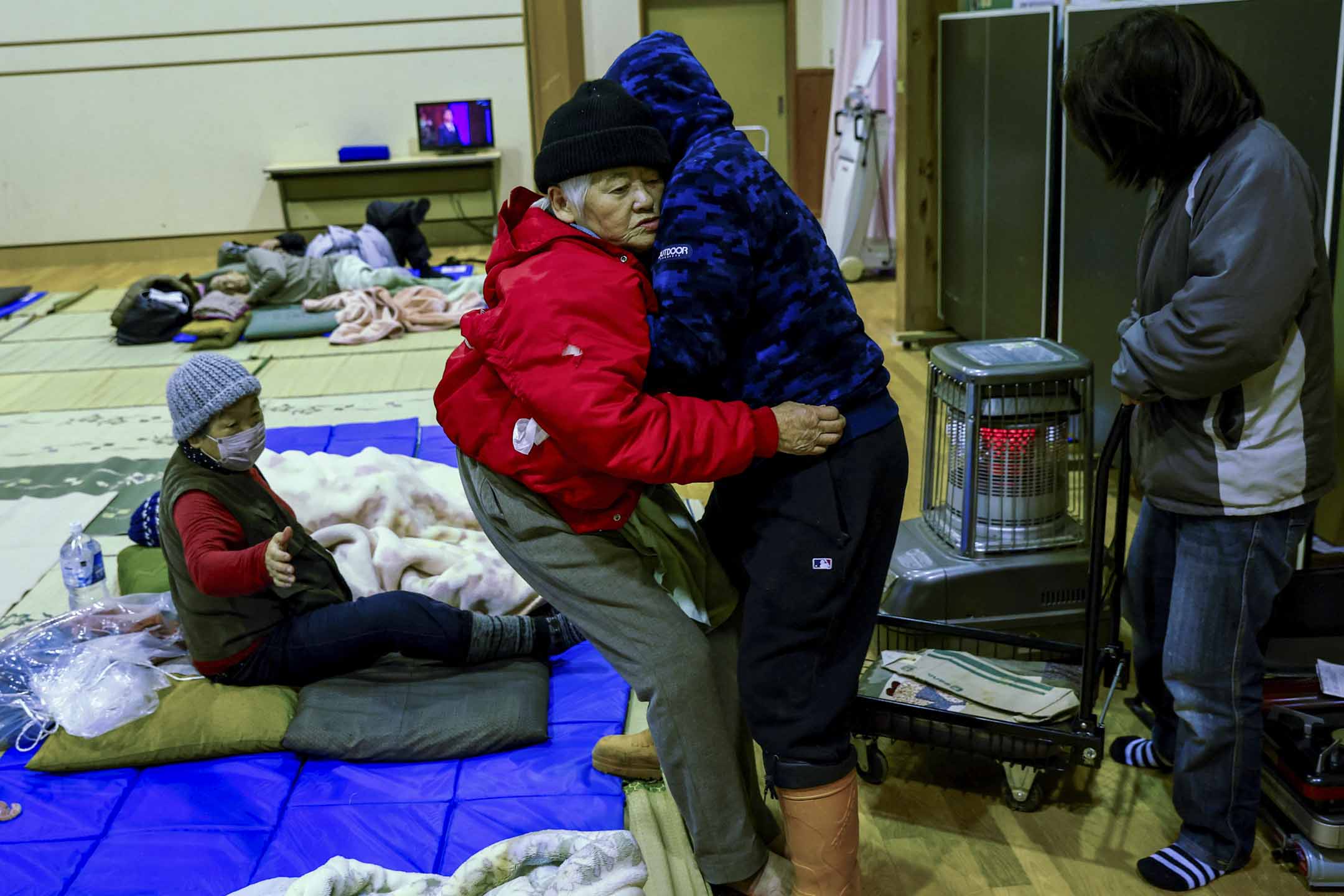 2024年1月2日,日本石川县轮岛,地震发生后,一名男子帮助他的母亲躺在社区中心的床垫上,该社区中心已改建成疏散中心。摄:Kim Kyung-Hoon/Reuters/达志影像