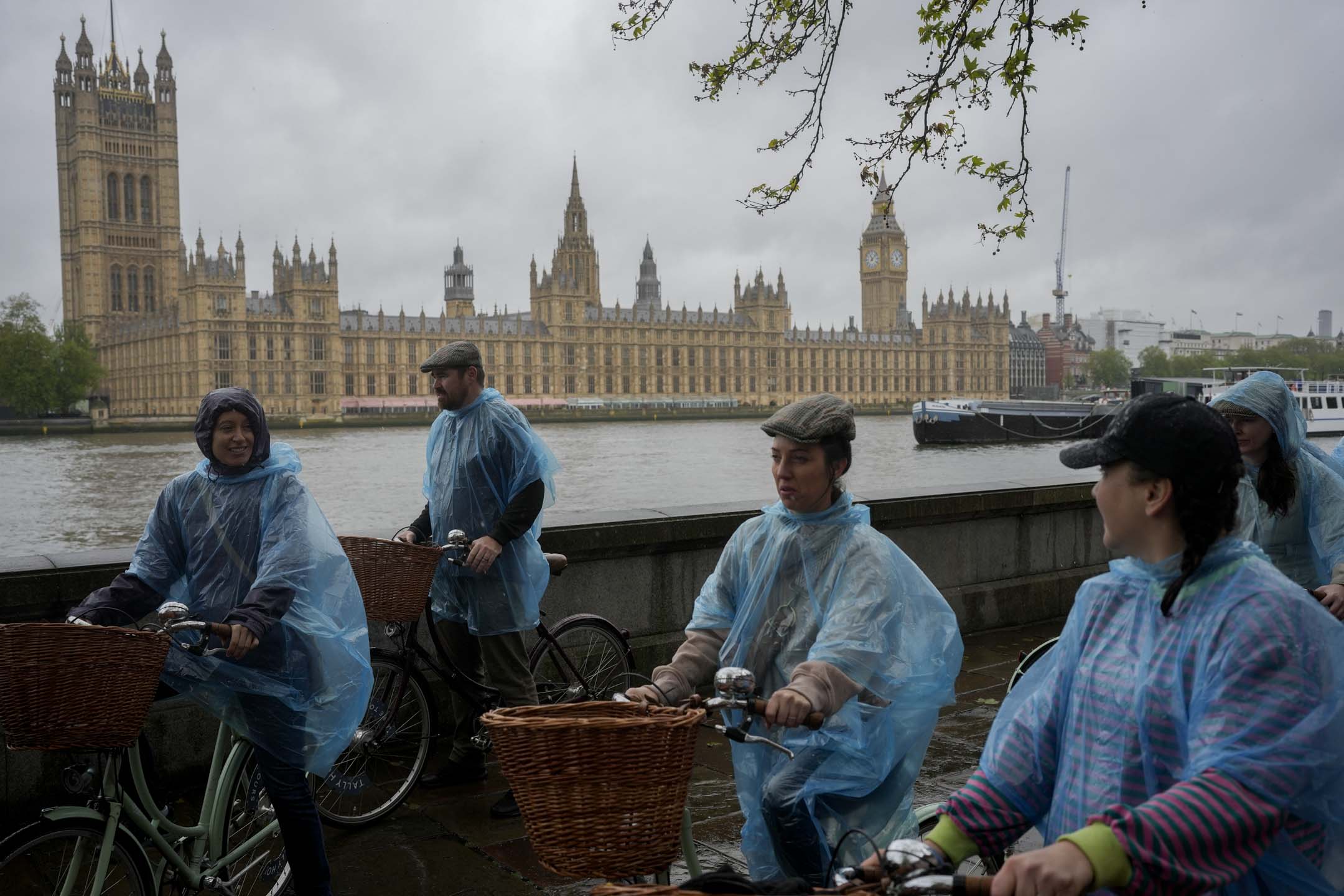 2024年5月3日,英国伦敦,游人穿著潮湿的塑胶雨伞骑自行车游览议会大厦。摄:Kin Cheung/AP/达志影像