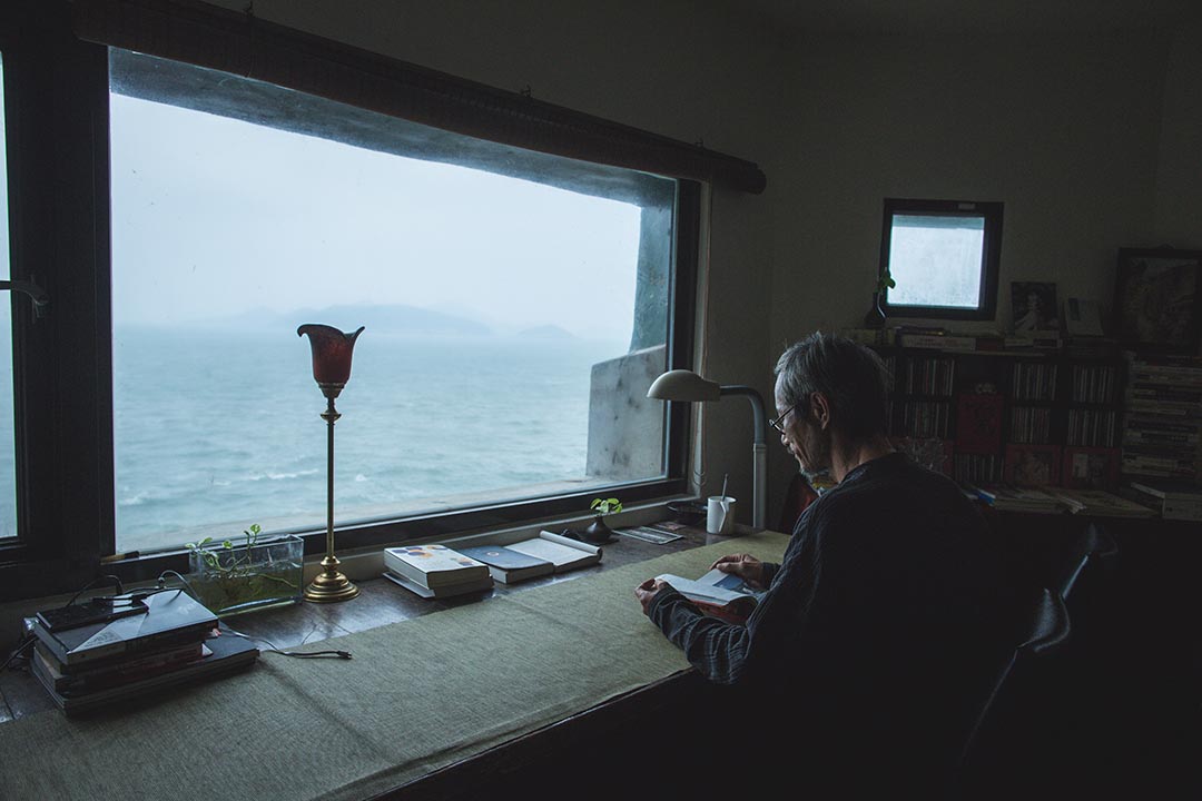 面向海邊,在書房看書的刺鳥咖啡館負責人曹以雄。攝:王嘉豪/端傳媒